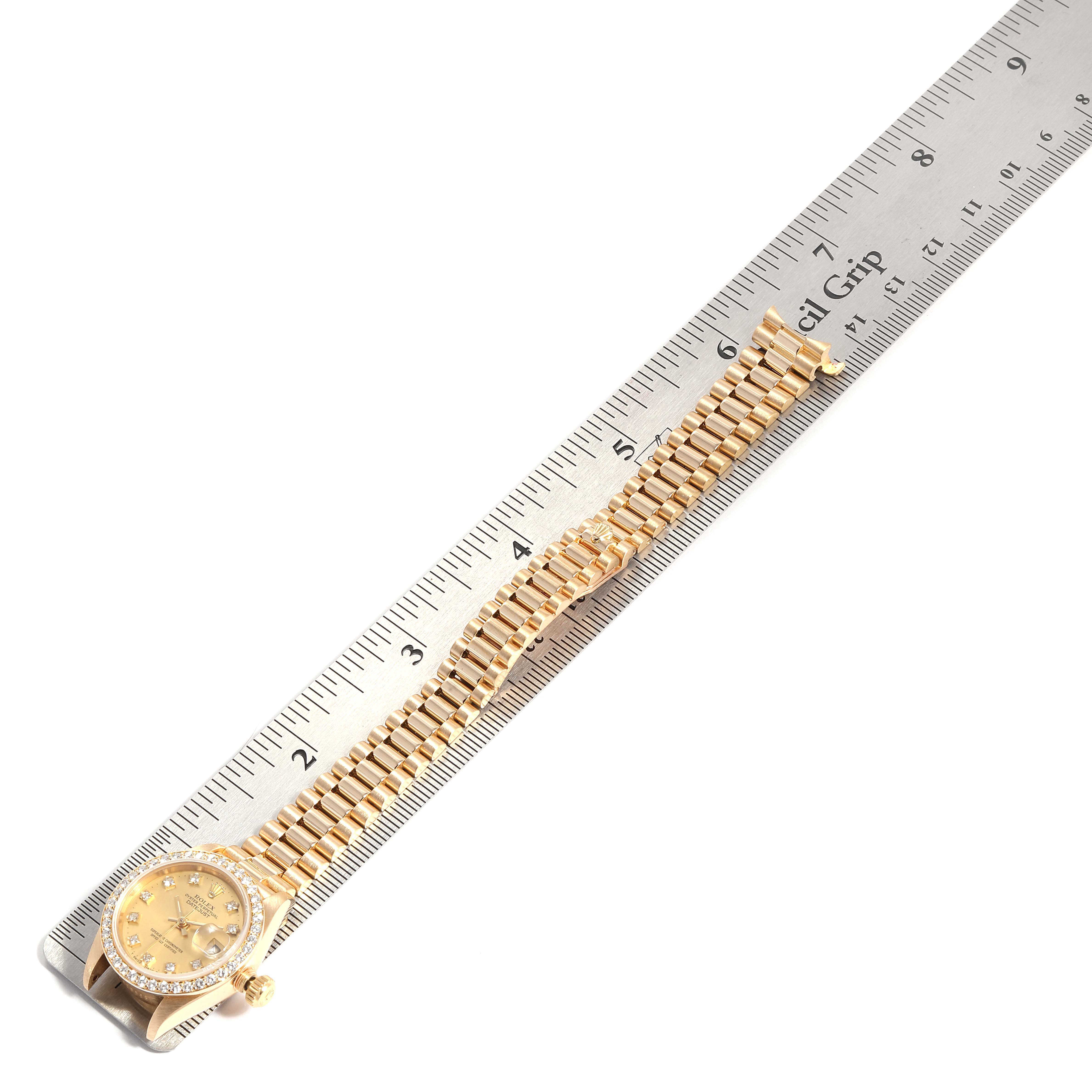 The image shows a Rolex President 69138 Women
s Yellow Gold Champagne Dial 69138 Women
s Yellow Gold Champagne Dial model watch placed next to a ruler, displaying the face and bracelet from a top-down angle.