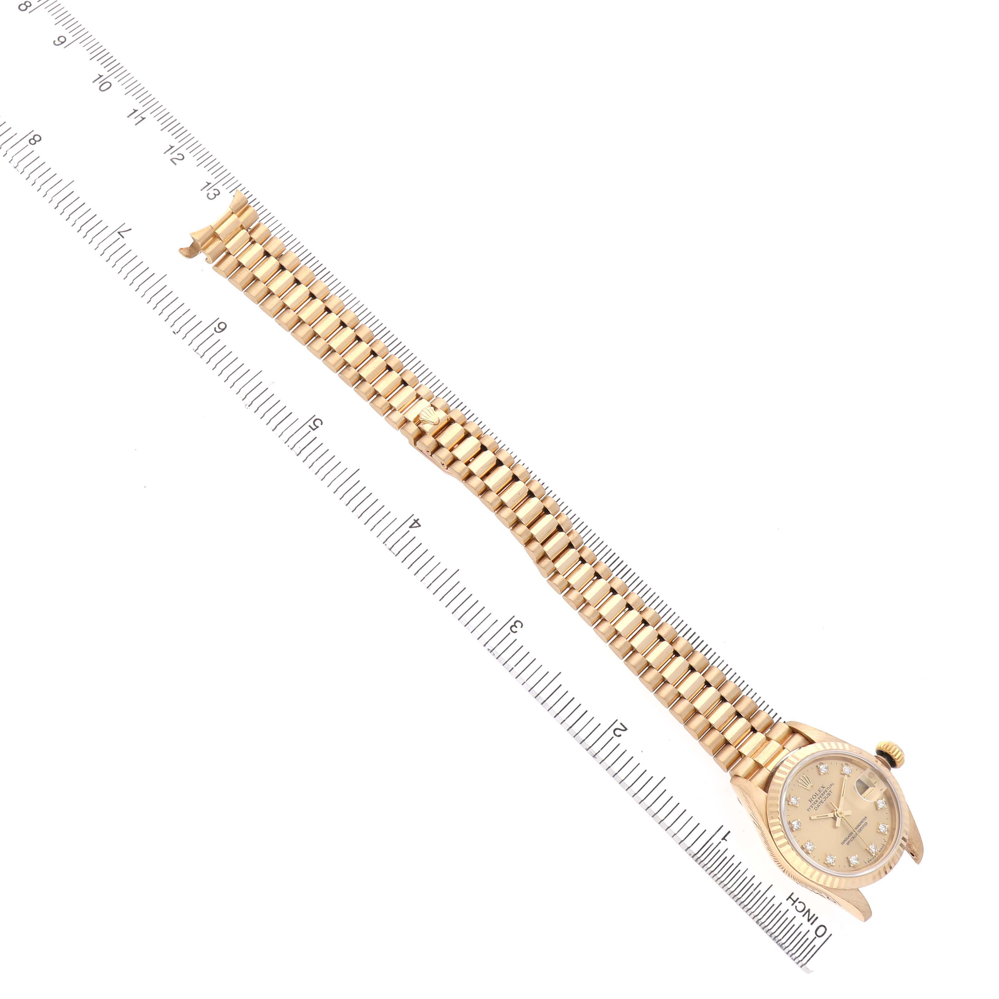 The image shows a Rolex President 69178 Women's Yellow Gold Champagne Dial watch at a top-down angle, highlighting the gold bracelet and diamond-set dial next to a ruler.
