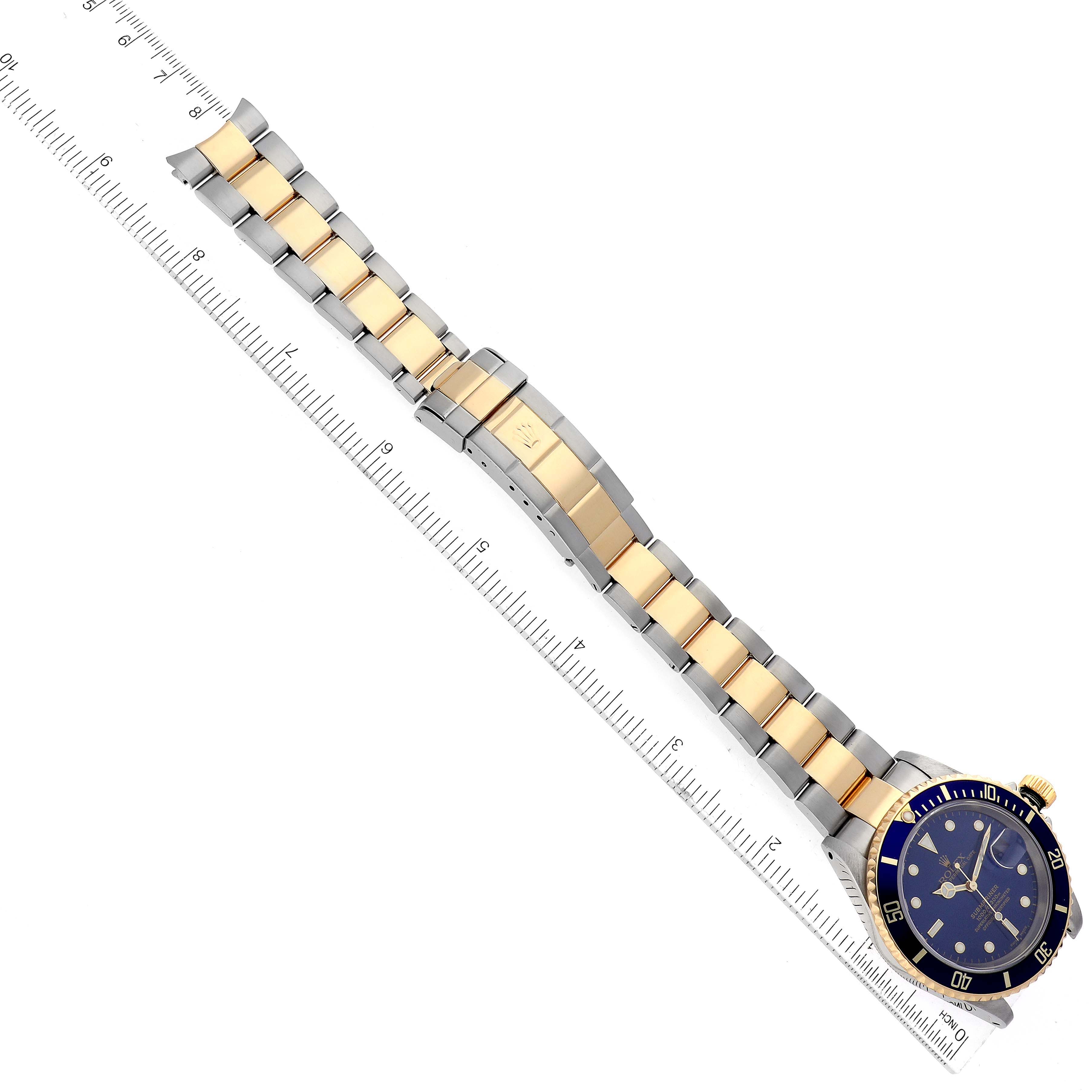 The image shows a top-down view of a Rolex Submariner 16613 Men's Steel and Gold (two tone) Blue Dial 16613 Men's Steel and Gold (two tone) Blue Dial watch, highlighting the blue dial, bezel, and two-tone metal bracelet with a ruler for scale.