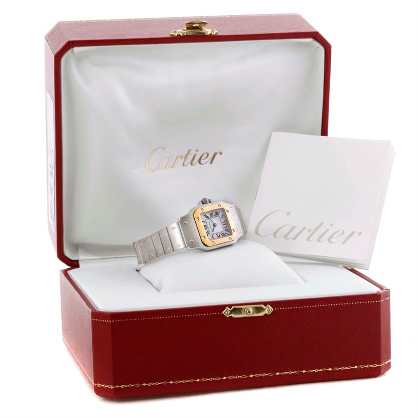 The Cartier Santos W20012C4 Women
s Stainless Steel Silver Dial W20012C4 Women
s Stainless Steel Silver Dial watch is shown in an open, red Cartier box, alongside a booklet with "Cartier" on the cover.
