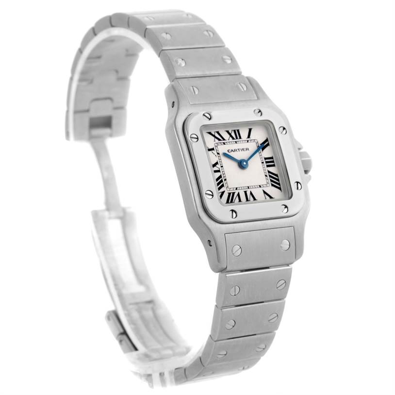 The image shows a Cartier Santos W20056D6 Women
s Stainless Steel Silver Dial W20056D6 Women
s Stainless Steel Silver Dial watch at a tilted angle, highlighting its square face, Roman numerals, and metal strap with screws.