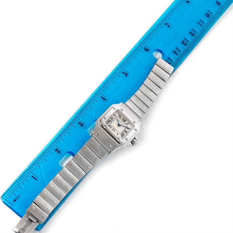 The Santos de Cartier watch is displayed flat, showing the face, bezel, and entire bracelet alongside a blue ruler for scale.