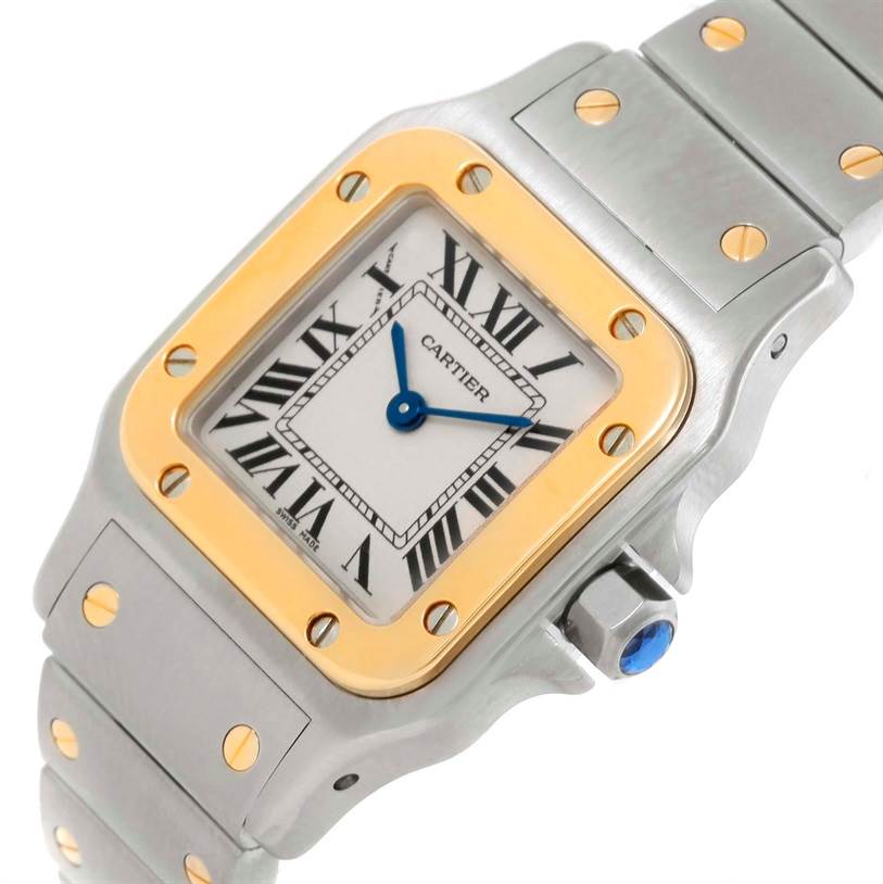 The Cartier Santos W20012C4 Women
s Stainless Steel Silver Dial W20012C4 Women
s Stainless Steel Silver Dial watch is shown at an angled view, highlighting its square face, Roman numerals, metal bracelet, and gold bezel.