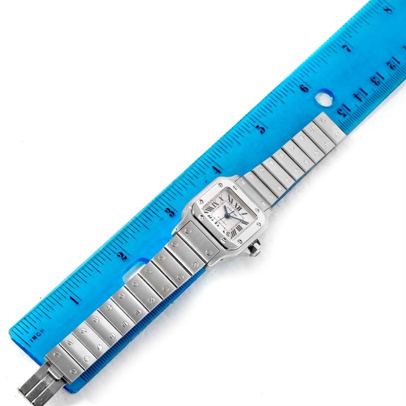The Cartier Santos W20054D6 Women
s Stainless Steel Silver Dial W20054D6 Women
s Stainless Steel Silver Dial watch is shown from a top-down angle with the band and face fully visible alongside a ruler for size reference.