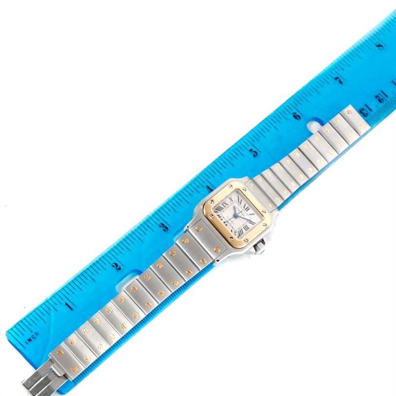 The Cartier Santos W20057C4 Women
s Stainless Steel Silver Dial W20057C4 Women
s Stainless Steel Silver Dial watch is shown from a top-down view with its entire band and face visible next to a blue ruler.