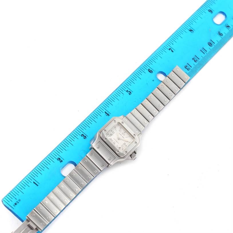The image shows a top-down view of a Cartier Santos W20044D6 Women
s Stainless Steel Silver Dial W20044D6 Women
s Stainless Steel Silver Dial watch placed next to a blue ruler for scale measurement.