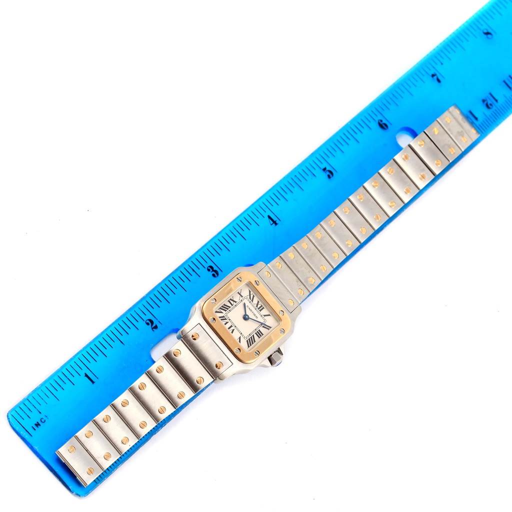 The Cartier Santos W20012C4 Women
s Stainless Steel Silver Dial W20012C4 Women
s Stainless Steel Silver Dial watch is displayed flat with its face and metal band visible, alongside a blue ruler for size reference.