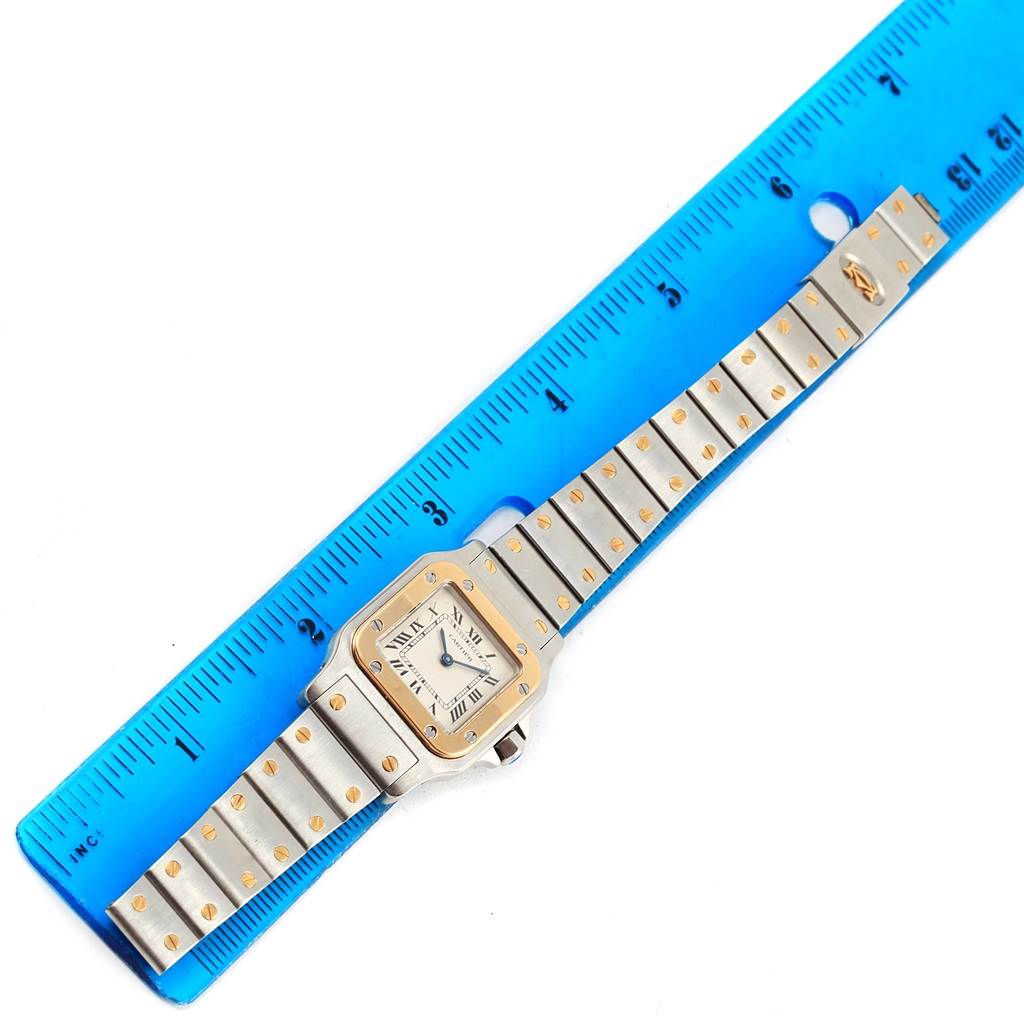 The image shows an overhead view of a Cartier Santos 166930 Women
s Stainless Steel Silver Dial 166930 Women
s Stainless Steel Silver Dial watch next to a blue ruler for scale.