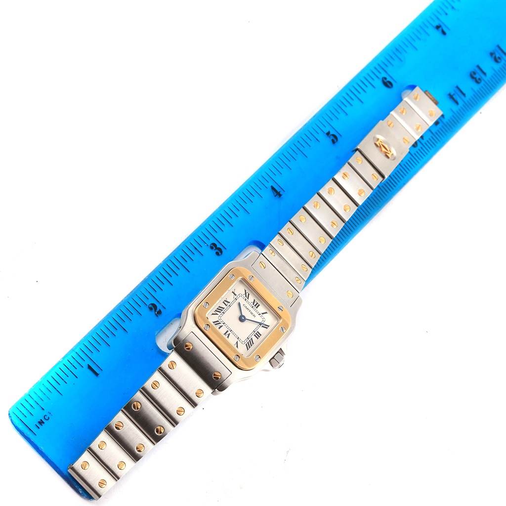The image shows a Cartier Santos 166930 Women's Stainless Steel Silver Dial 166930 Women's Stainless Steel Silver Dial watch placed next to a blue ruler, displaying its face and bracelet.