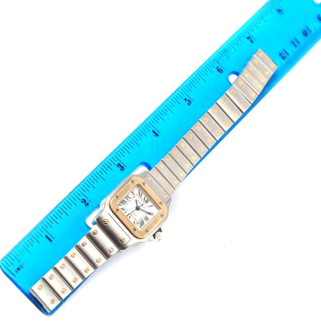 The image shows a Santos model watch by Cartier laid flat next to a blue ruler for measurement.