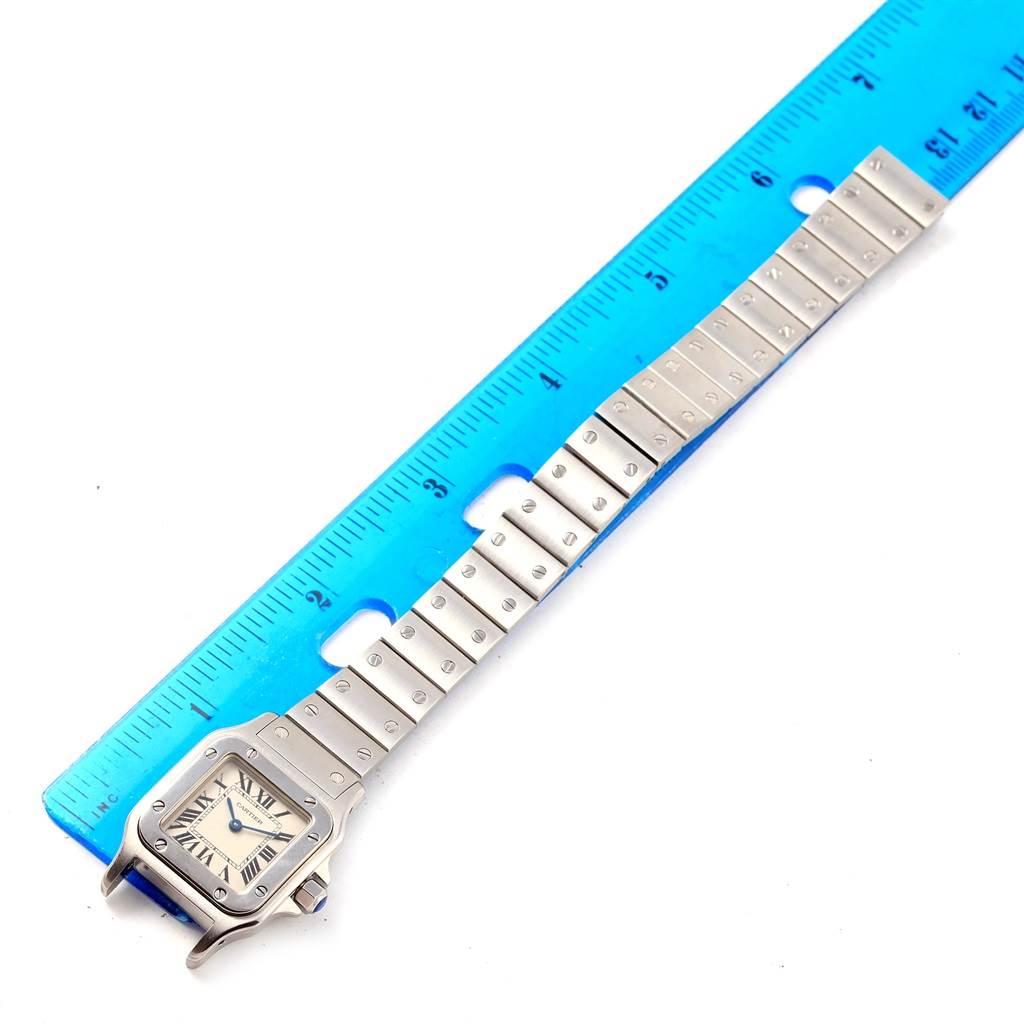 The image shows a top-down view of a Cartier Santos W20056D6 Men's Stainless Steel Silver Dial W20056D6 Men's Stainless Steel Silver Dial watch alongside a blue ruler.