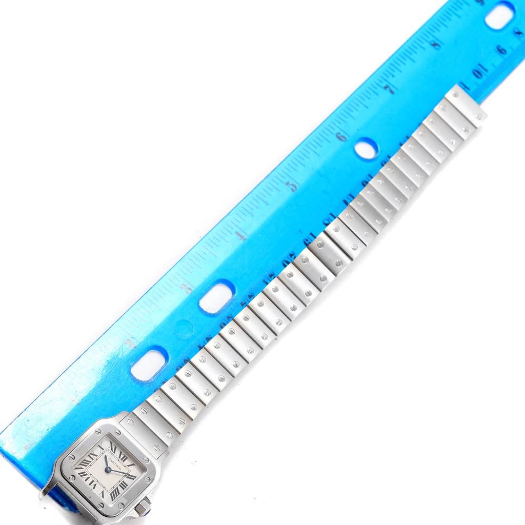 The image shows the Santos model watch by Cartier, displaying the face and entire bracelet laid next to a ruler for measurement.