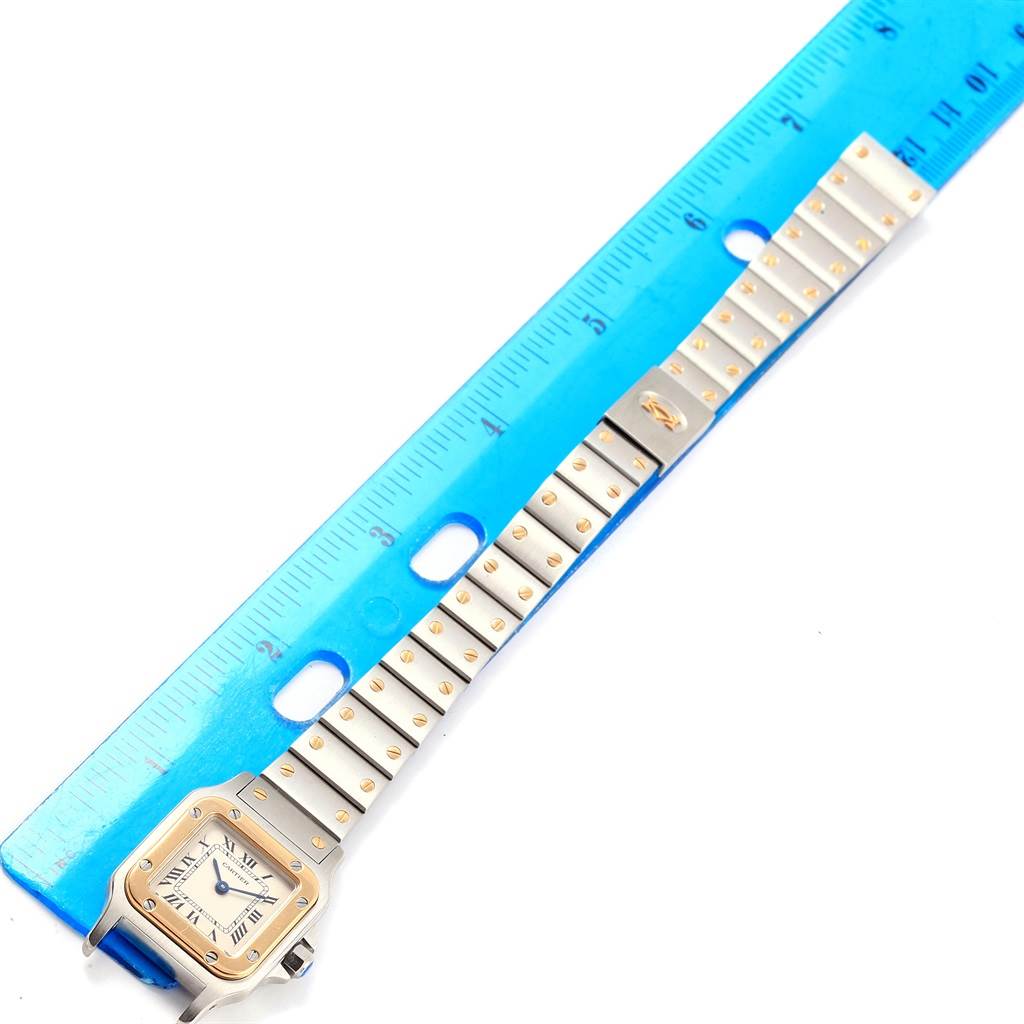 The image shows a Santos model watch by Cartier from an angled top view, positioned next to a blue ruler, including both the dial and bracelet.