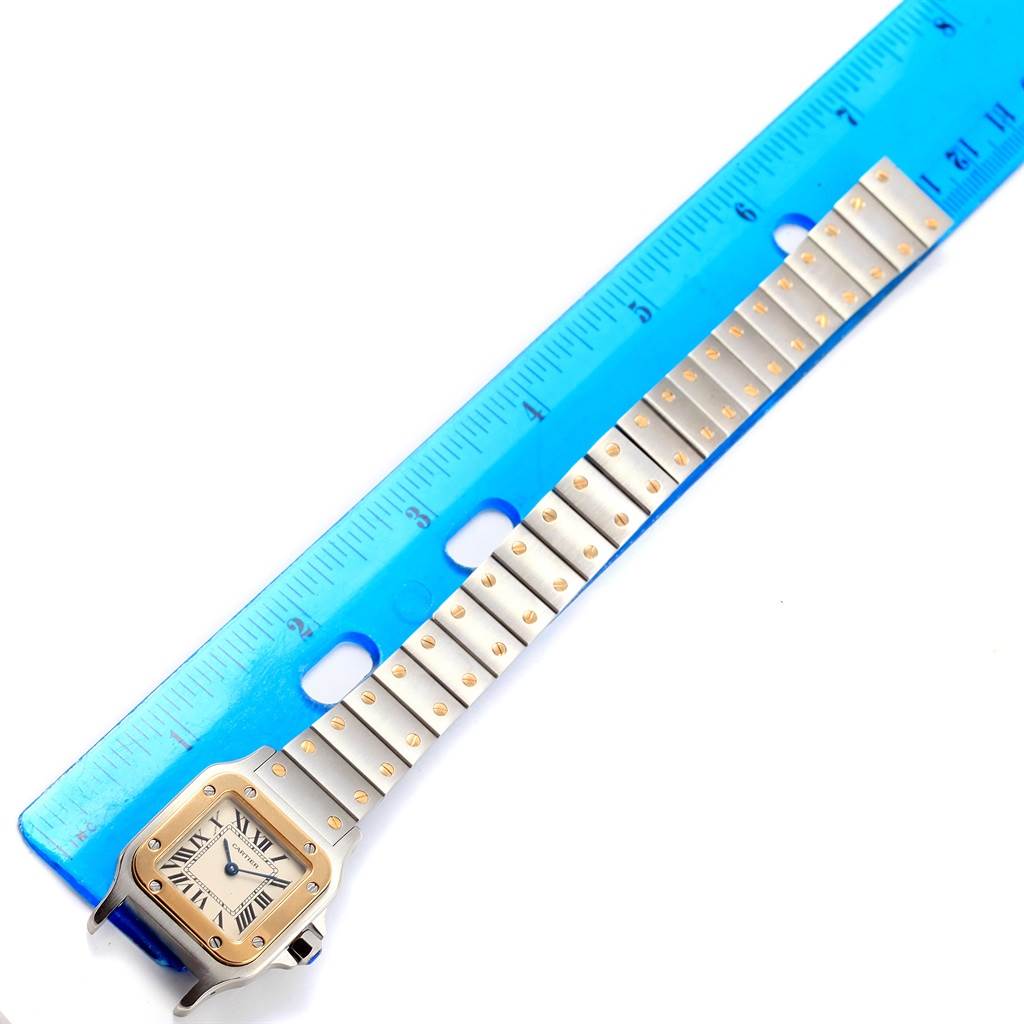 The Cartier Santos W20012C4 Women's Stainless Steel Silver Dial W20012C4 Women's Stainless Steel Silver Dial watch is shown from the top, highlighting its strap, face, and measured against a blue ruler.