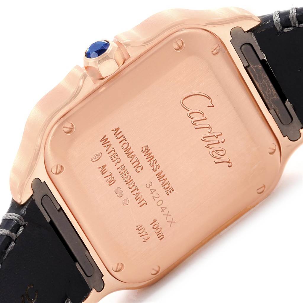 The image shows the back case and part of the strap of a Cartier Santos WGSA0012 Women's Rose Gold Silver Dial WGSA0012 Women's Rose Gold Silver Dial model watch, highlighting its inscriptions and crown.