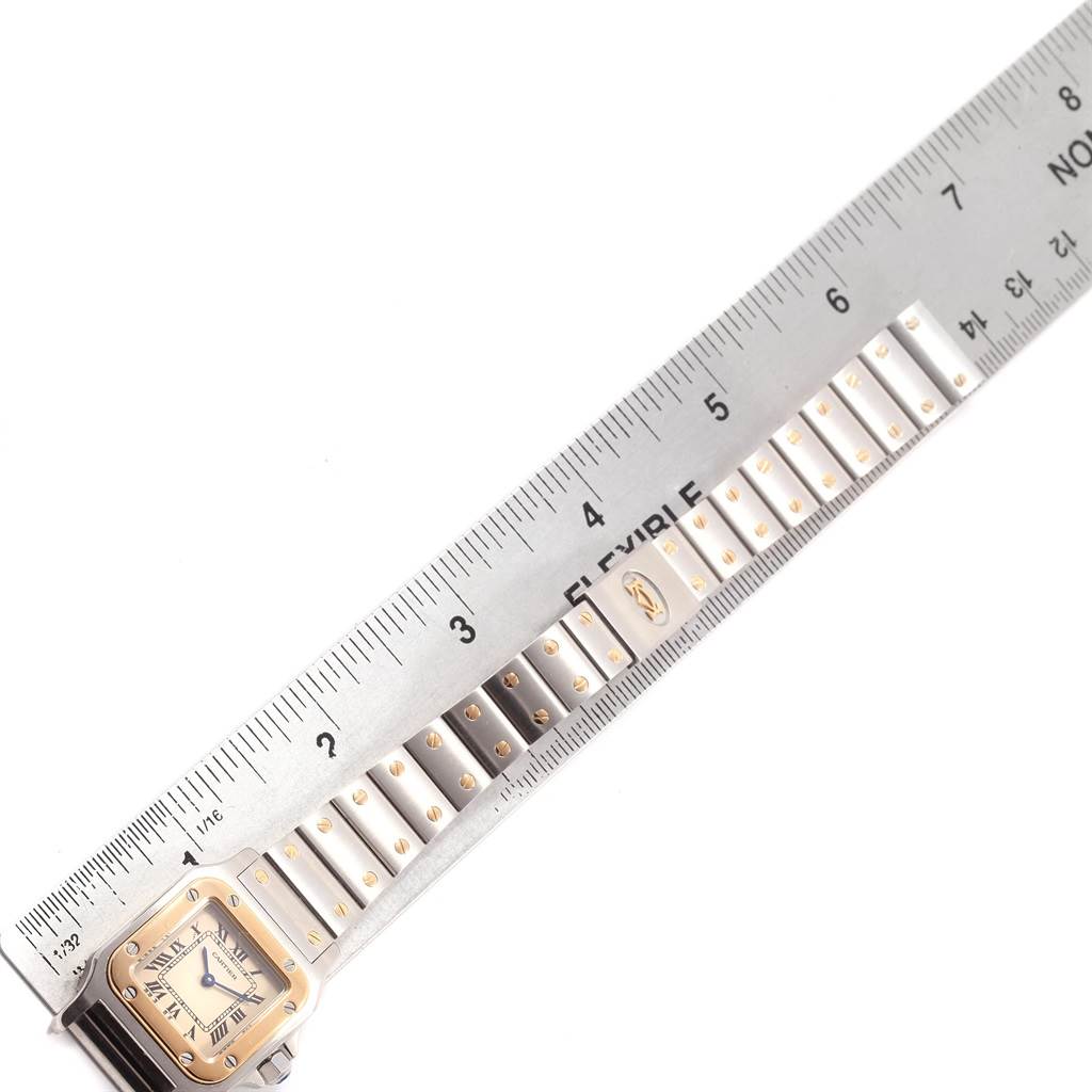 The image shows a close-up of the Santos model by Cartier watch face and metal strap, placed next to a ruler.