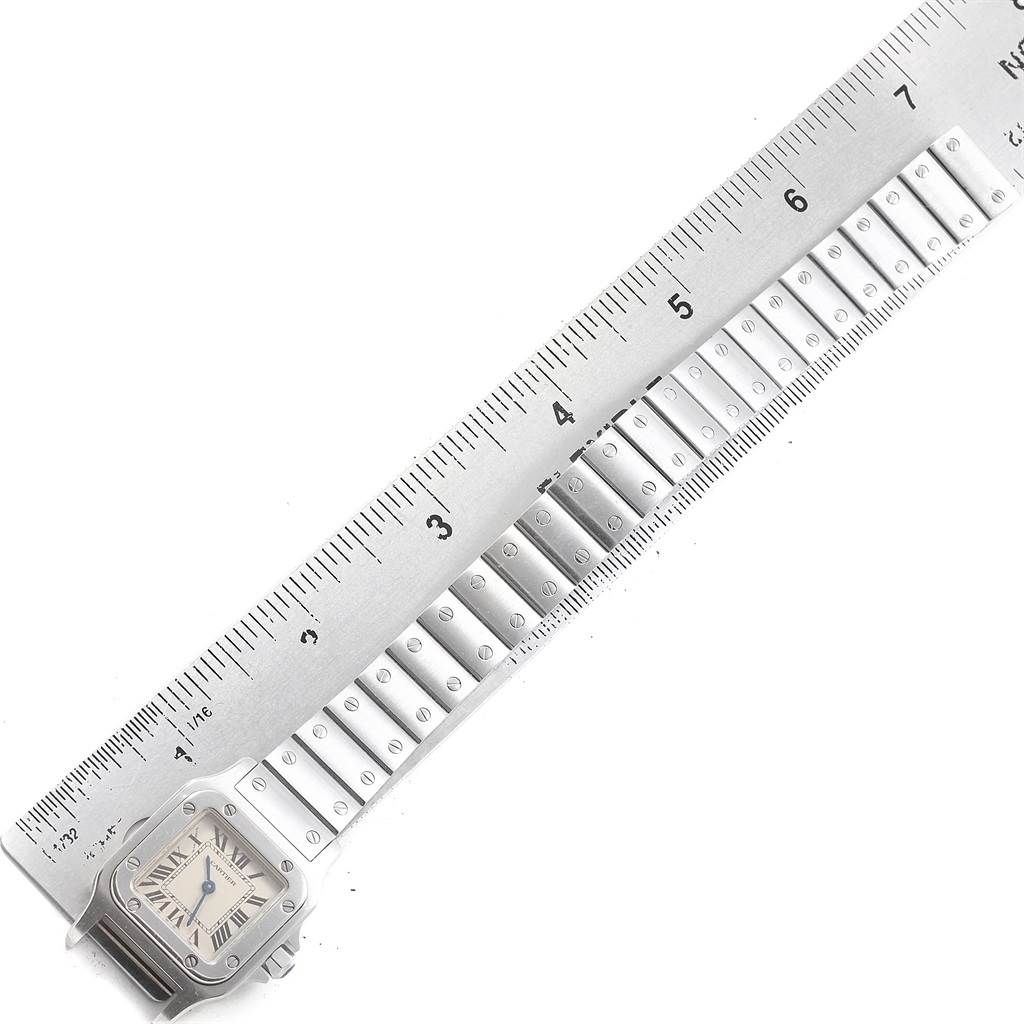 The image shows a close-up of a Santos model by Cartier, highlighting the watch face and a section of its metal bracelet.