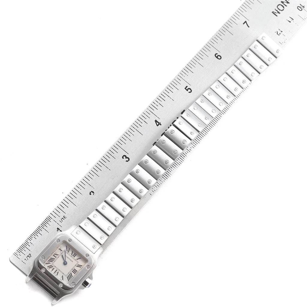 The image shows a top-down view of a Santos by Cartier watch, highlighting its face, part of the bracelet, and a ruler measuring it.