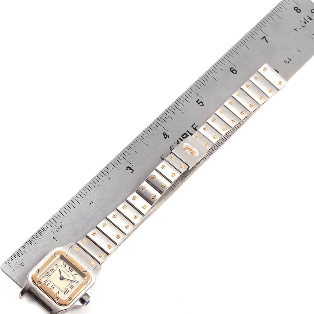 This image shows the Cartier Santos 1057930 Women's Stainless Steel Silver Dial 1057930 Women's Stainless Steel Silver Dial watch lying flat next to a ruler, displaying its face, bracelet, and some details of its band.