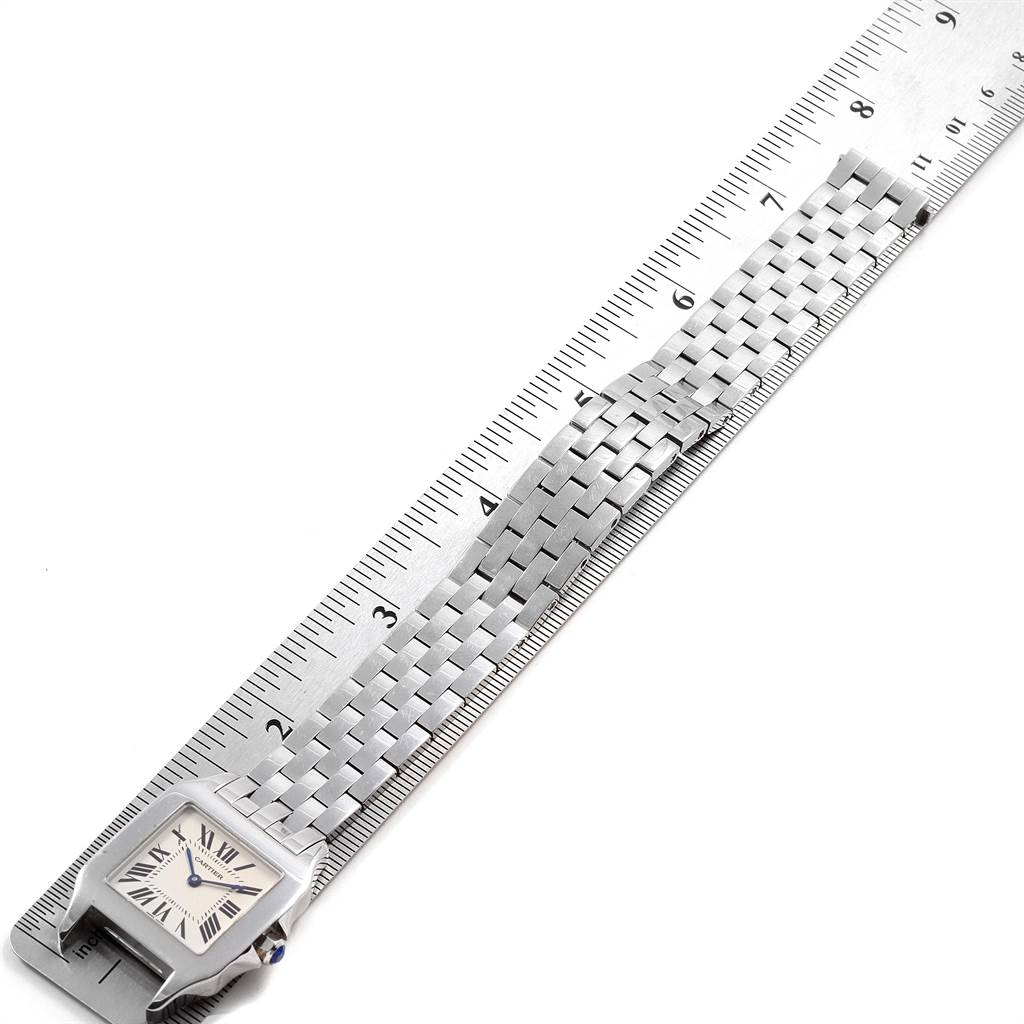 The image shows a partial view of a Santos model by Cartier, displaying the watch face, metal strap, and a ruler for measurement.