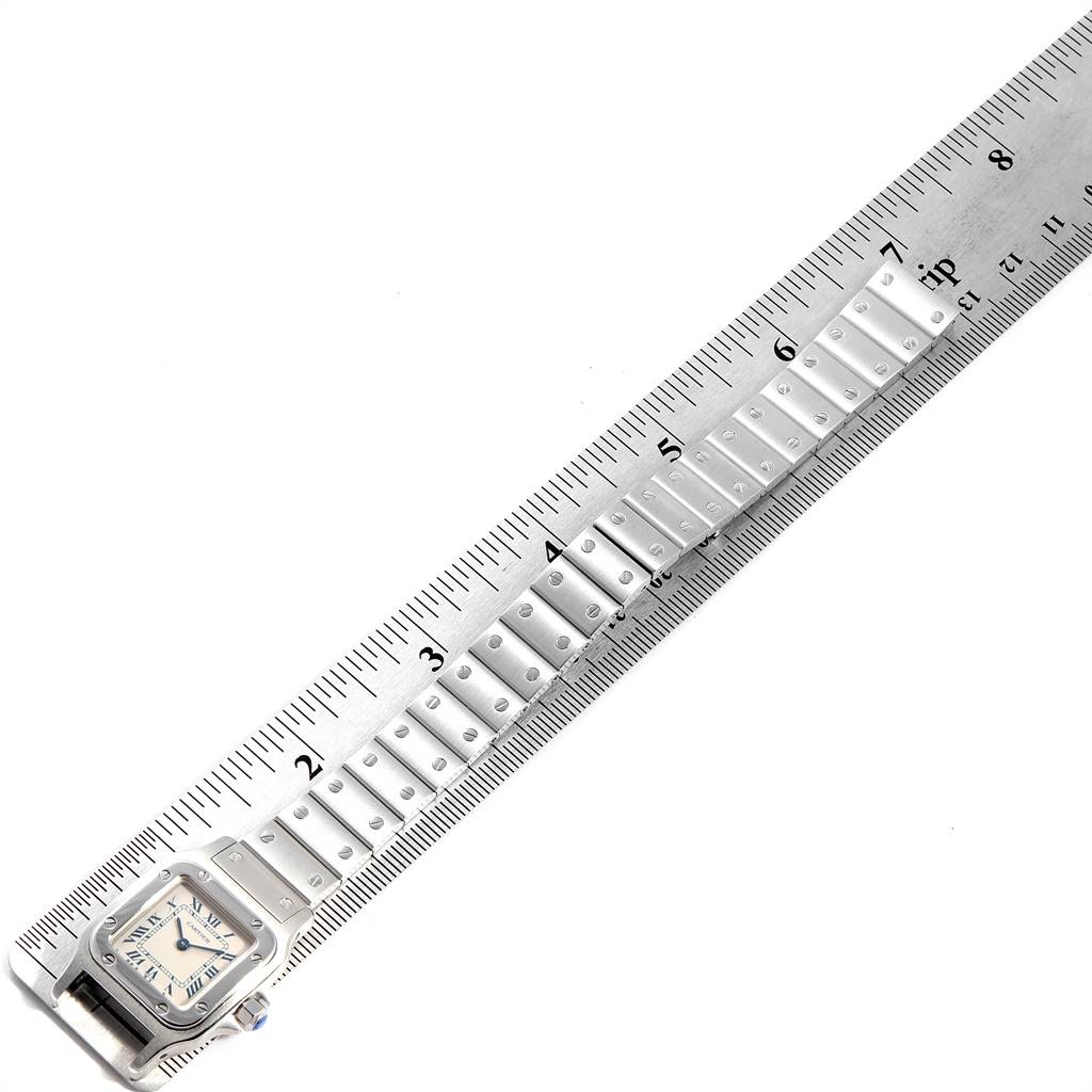 The image shows a Cartier Santos 1565 Women's Stainless Steel Silver Dial 1565 Women's Stainless Steel Silver Dial watch laid flat beside a ruler, displaying its band and face from a top-down angle.