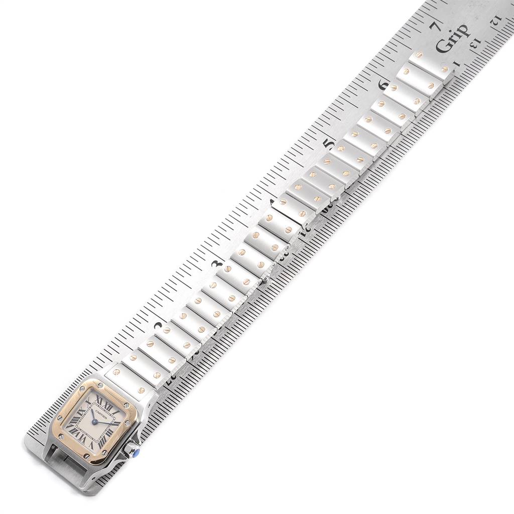 The image shows a top view of a Santos by Cartier watch, highlighting the face and full metal bracelet and laid alongside a ruler.