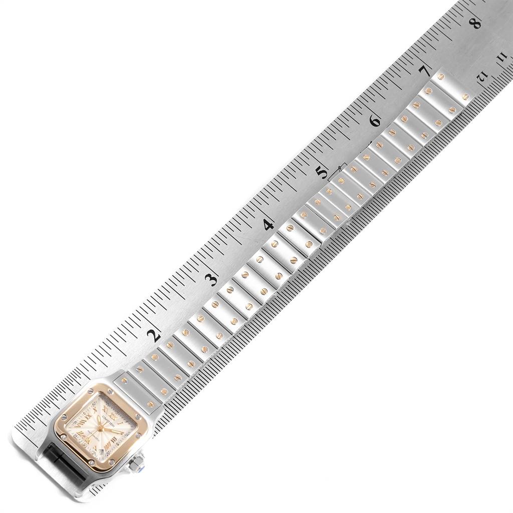The image shows a Santos model by Cartier from an overhead angle, displaying the face and a portion of the metal bracelet alongside a ruler.