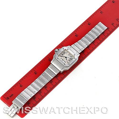 The image shows a Cartier Santos W20054D6 Women
s Stainless Steel Silver Dial W20054D6 Women
s Stainless Steel Silver Dial watch, laid flat on a red ruler, displaying the face and metal bracelet completely.