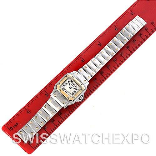 The image shows a top-down view of a Santos model Cartier watch placed on a red ruler.