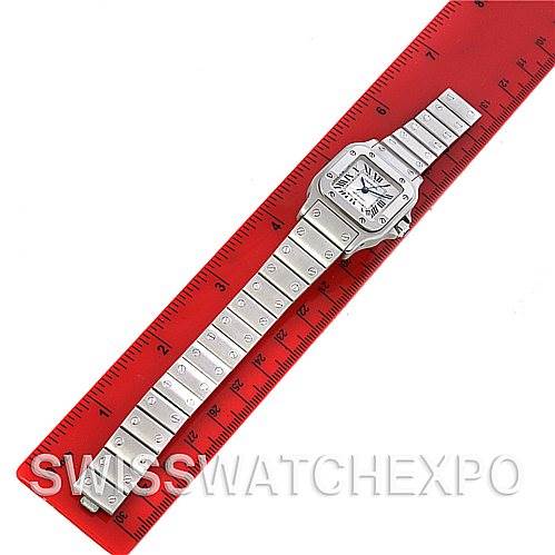 This image shows a Cartier Santos W20054D6 Women
s Stainless Steel Silver Dial W20054D6 Women
s Stainless Steel Silver Dial watch laid flat against a red ruler, showcasing its face and metal bracelet.
