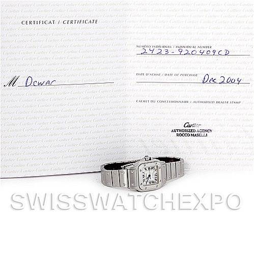 The Cartier Santos W20054D6 Women
s Stainless Steel Silver Dial W20054D6 Women
s Stainless Steel Silver Dial watch is displayed lying flat next to a certificate, showing its face and part of the bracelet.
