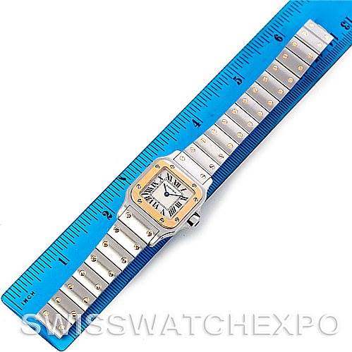 This image shows a top-down view of a Cartier Santos W20012C4 Women
s Stainless Steel Silver Dial W20012C4 Women
s Stainless Steel Silver Dial watch, with its face and full band next to a blue ruler for scale.