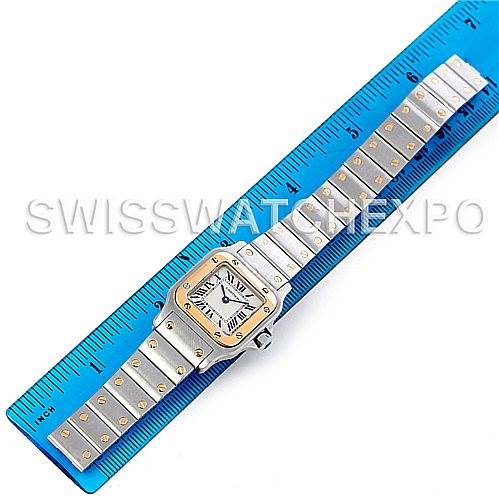 The Cartier Santos W20012C4 Women
s Stainless Steel Silver Dial W20012C4 Women
s Stainless Steel Silver Dial watch is displayed flat on a blue ruler, showing the face with Roman numerals and the bracelet with gold accents.