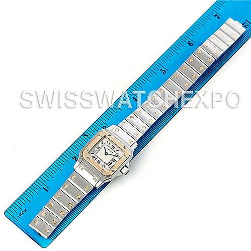 The image shows a top-down view of a Cartier Santos W20012C4 Women
s Stainless Steel Silver Dial W20012C4 Women
s Stainless Steel Silver Dial watch, displaying its face and metal bracelet alongside a blue measuring ruler.