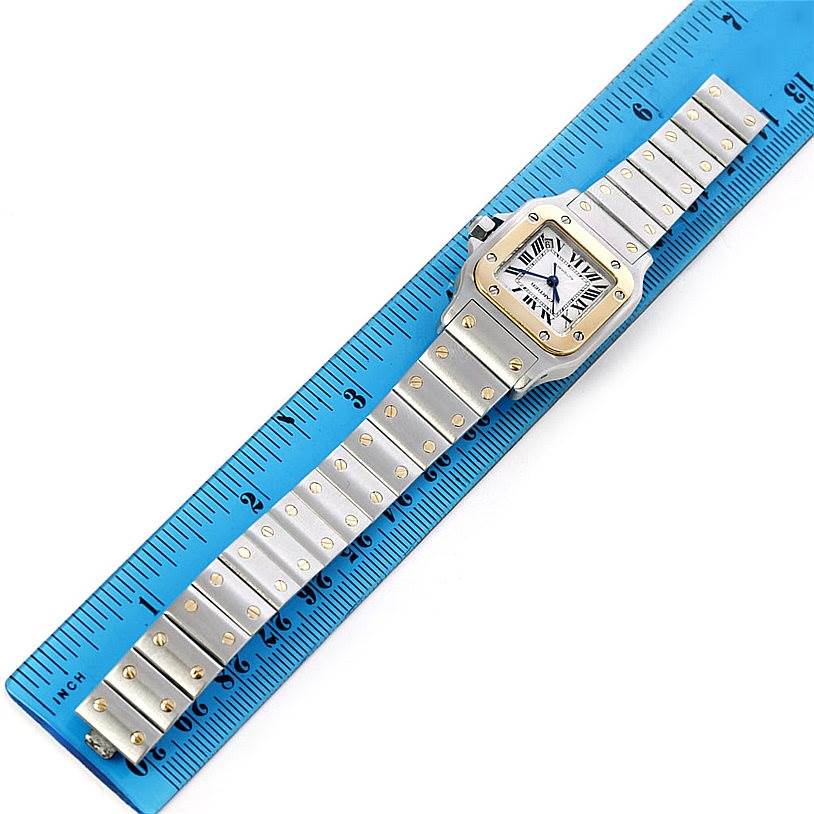 The Cartier Santos W20045C4 Women
s Stainless Steel Silver Dial W20045C4 Women
s Stainless Steel Silver Dial watch is shown laid flat, displaying the face, case, and entire bracelet alongside a ruler for scale.