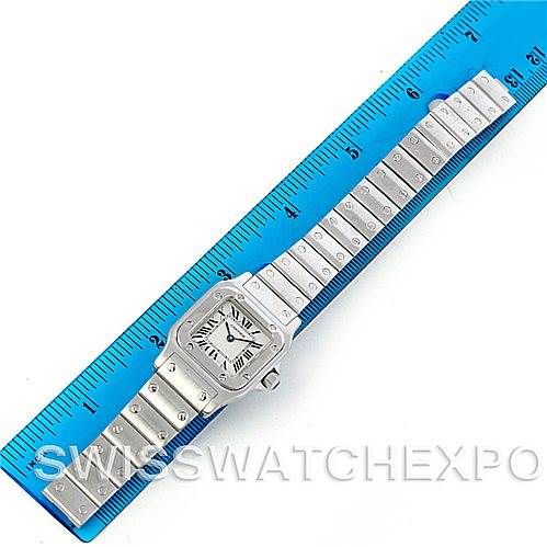 The image shows a top view of a Cartier Santos W20056D6 Women
s Stainless Steel Silver Dial W20056D6 Women
s Stainless Steel Silver Dial watch, including its face, bezel, and metal bracelet, alongside a ruler for scale.
