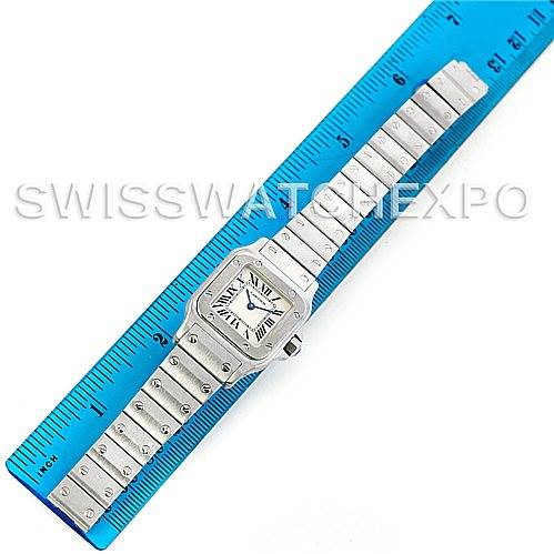 The image shows a Cartier Santos W20056D6 Women
s Stainless Steel Silver Dial W20056D6 Women
s Stainless Steel Silver Dial watch placed flat next to a blue ruler, displaying its face, bracelet, and clasp.