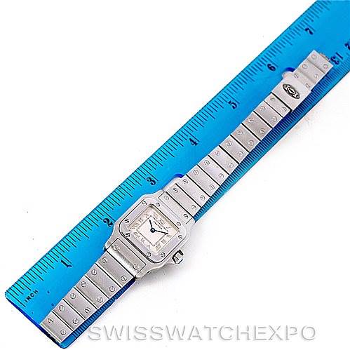 The watch, a Santos model by Cartier, is shown laid flat with its band extended next to a blue ruler.