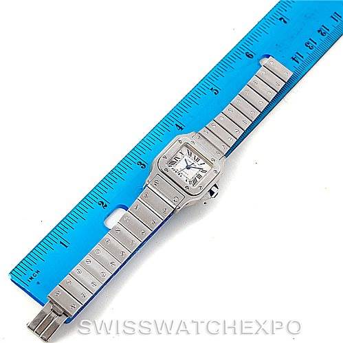 The image shows the Santos model by Cartier, featuring the watch face and full bracelet, set against a blue ruler for scale.