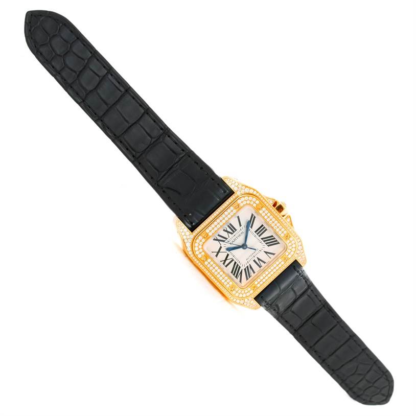 The Cartier Santos WM502051 Yellow Gold Silver Dial WM502051 Yellow Gold Silver Dial watch is shown at a top-down angle, highlighting its black leather strap and a diamond-encrusted gold bezel.