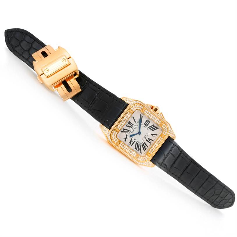 The Cartier Santos WM502051 Yellow Gold Silver Dial WM502051 Yellow Gold Silver Dial watch is shown at an angled top-down view, highlighting the black strap, rectangular face, and diamond-encrusted bezel.