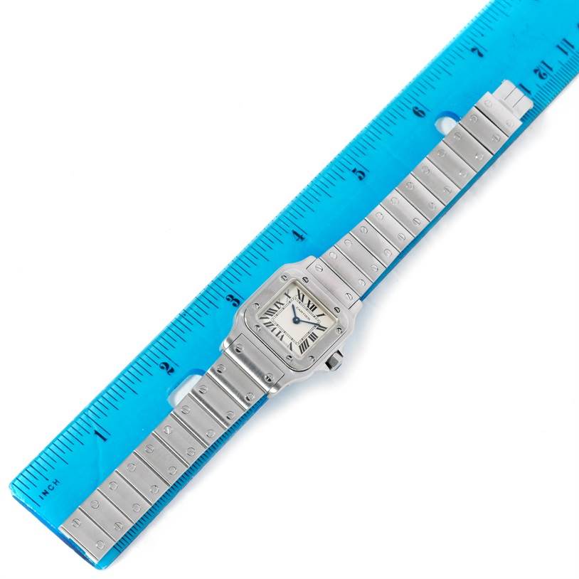 The image shows a Santos model watch by Cartier laid flat next to a blue ruler for measurement.