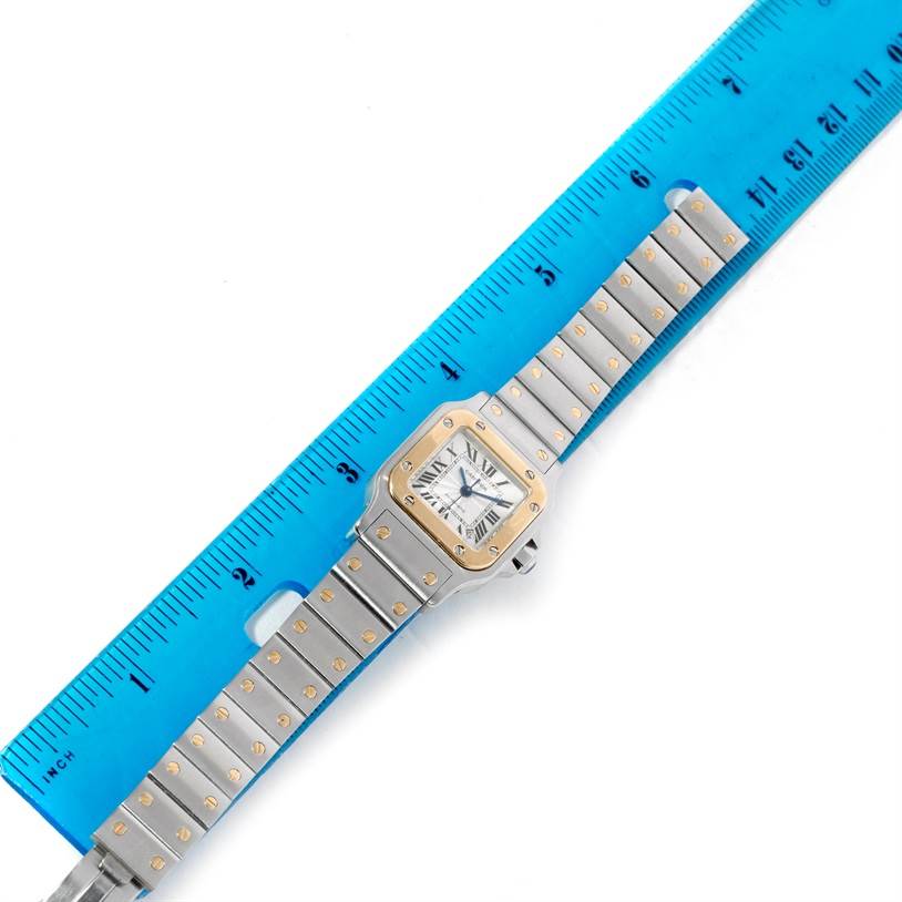 The image shows a top-down view of a Cartier Santos W20057C4 Women
s Stainless Steel Silver Dial W20057C4 Women
s Stainless Steel Silver Dial watch next to a blue ruler for measuring length.