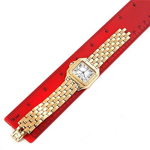 The image shows a Cartier Panthère watch laid flat on a red ruler, displaying its face and gold bracelet.