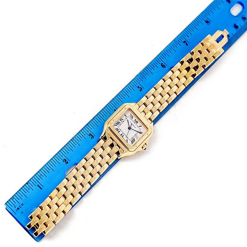 The Cartier Panthere W25014B9 Men's Yellow Gold Silver Dial W25014B9 Men's Yellow Gold Silver Dial watch is shown flat with its gold link bracelet beside a blue ruler for scale.