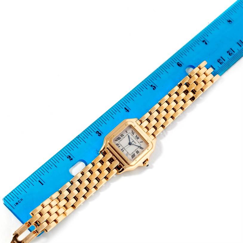 The Panthere model watch by Cartier is shown lying flat next to a blue ruler, displaying its face and gold bracelet.