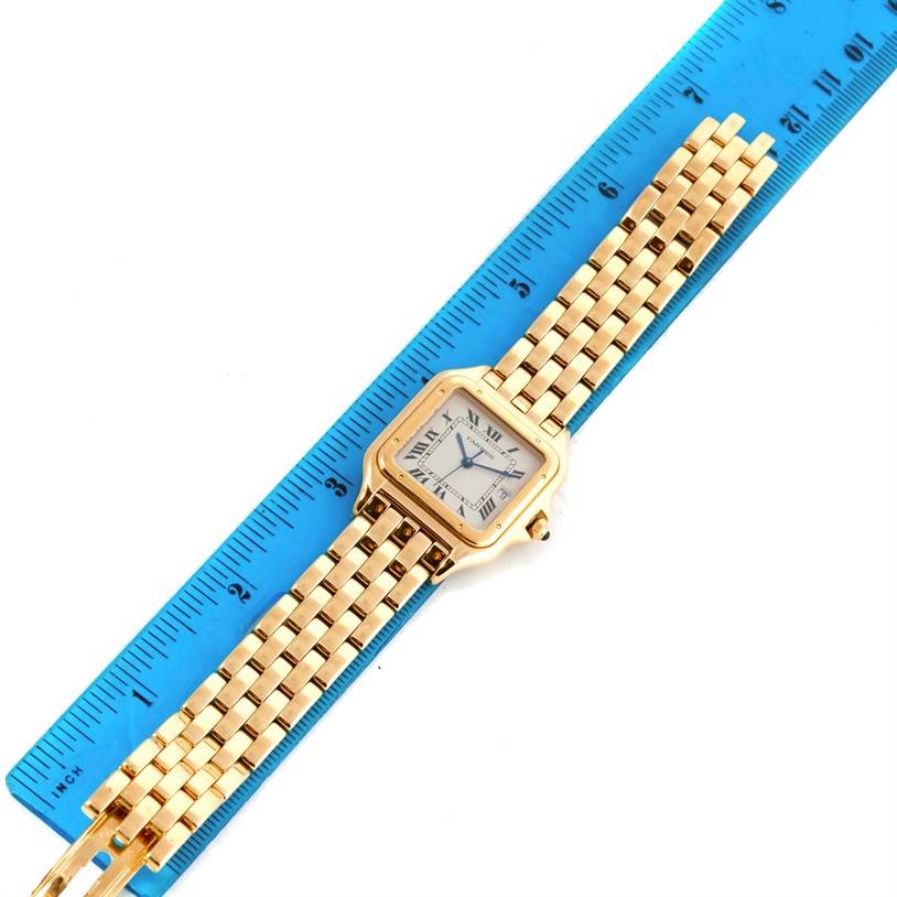 The image shows a top view of a Cartier Panthere W25014B9 Men's Yellow Gold Silver Dial W25014B9 Men's Yellow Gold Silver Dial watch with a gold band next to a blue ruler.