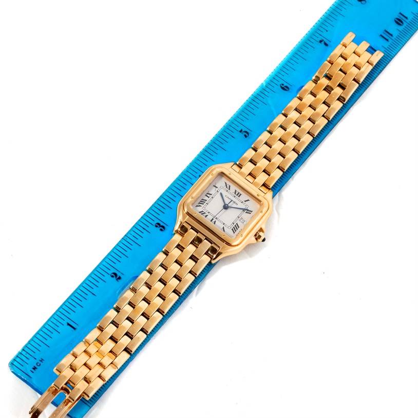 The image shows a top view of a Cartier Panthere W25014B9 Men's Yellow Gold Silver Dial W25014B9 Men's Yellow Gold Silver Dial watch with a gold band next to a blue ruler for scale.