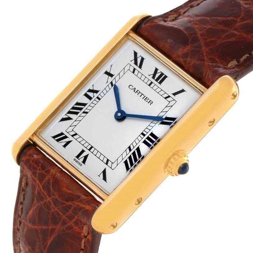 The image shows a Cartier Tank Classic Men
s Yellow Gold White Dial Men
s Yellow Gold White Dial model watch at a slight angle, displaying the Roman numeral dial, blue hands, gold case, and brown leather strap.