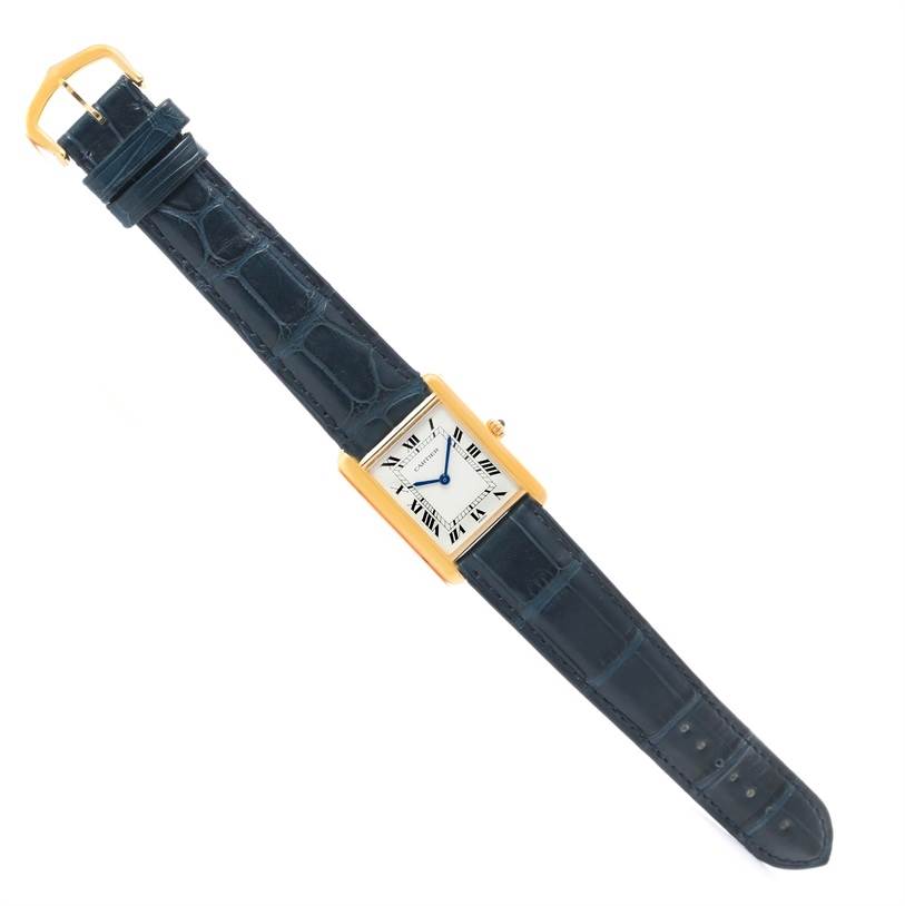 The image shows a Cartier Tank Classic Men's Yellow Gold White Dial Men's Yellow Gold White Dial watch laid flat, displaying the face, gold case, and blue leather strap vividly.